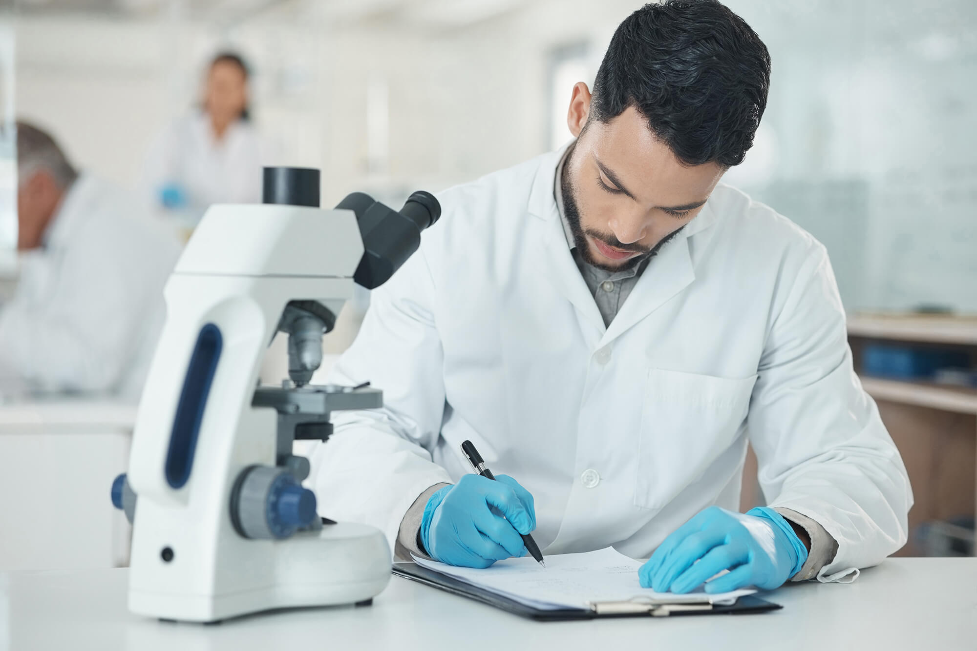 A scientist taking notes next to a microscope