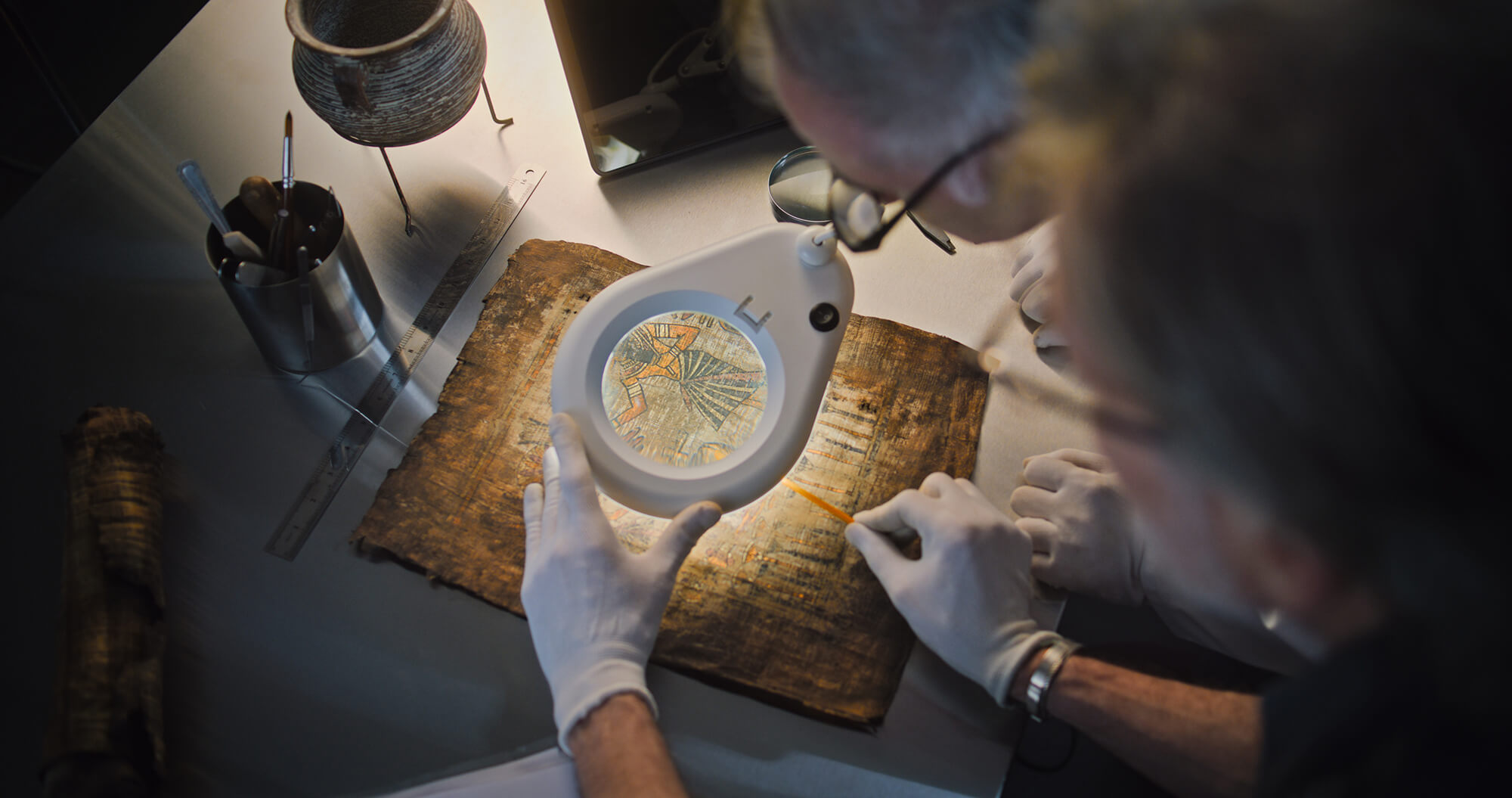 Close-up of papyrus being observed with a magnifying glass for authenticity analysis