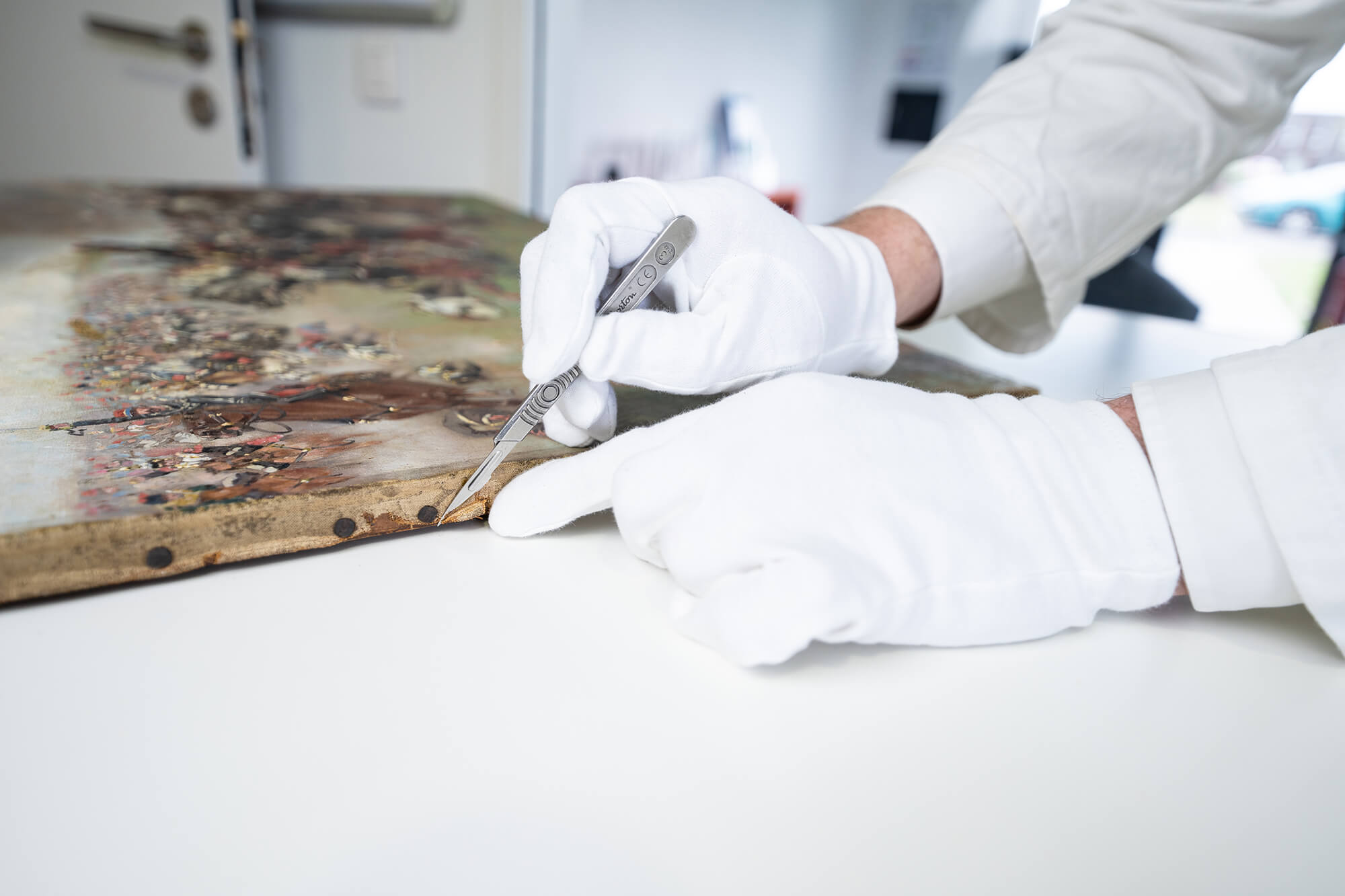 Close-up of a sample taken from a painting canvas with white gloves